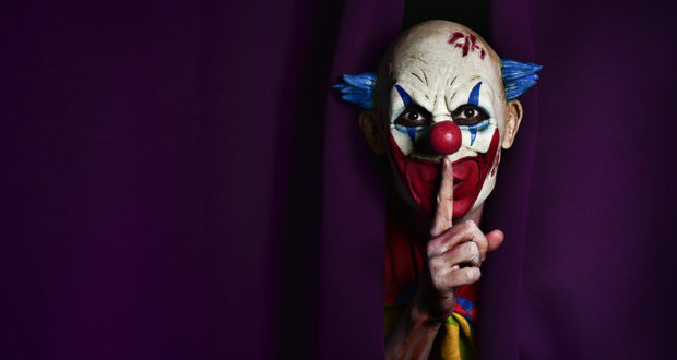 a scary evil clown peering out from a purple stage curtain, with