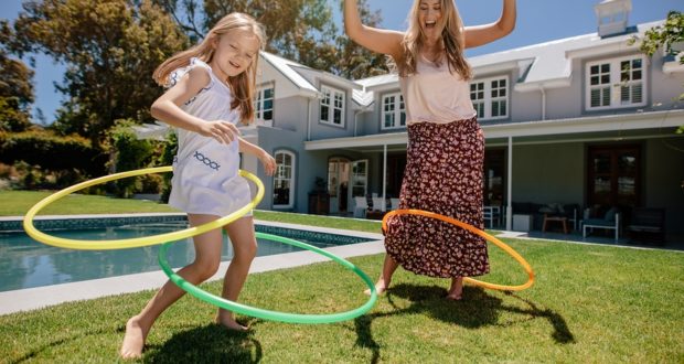 Mother And Daughter Playing With Hula Hoop In Their Backyard